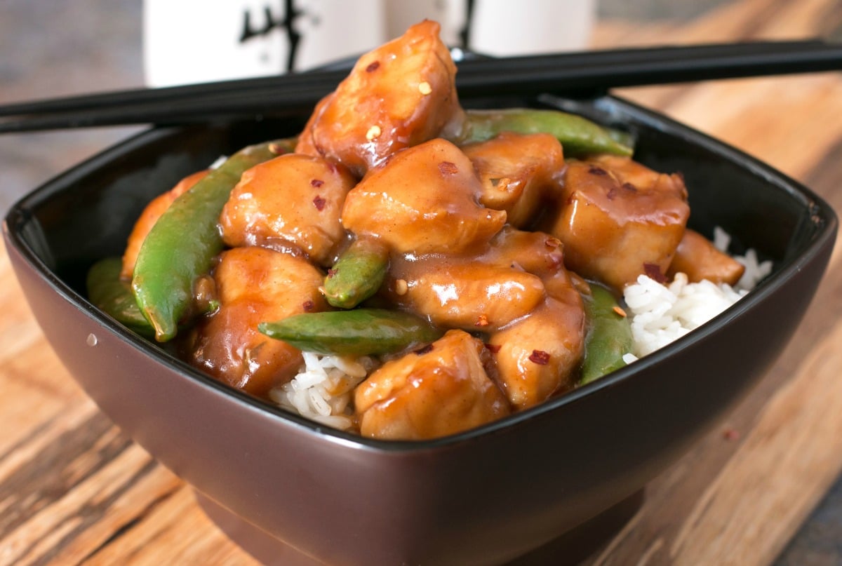 A black bowl filled with orange chicken recipe with snap peas and rice