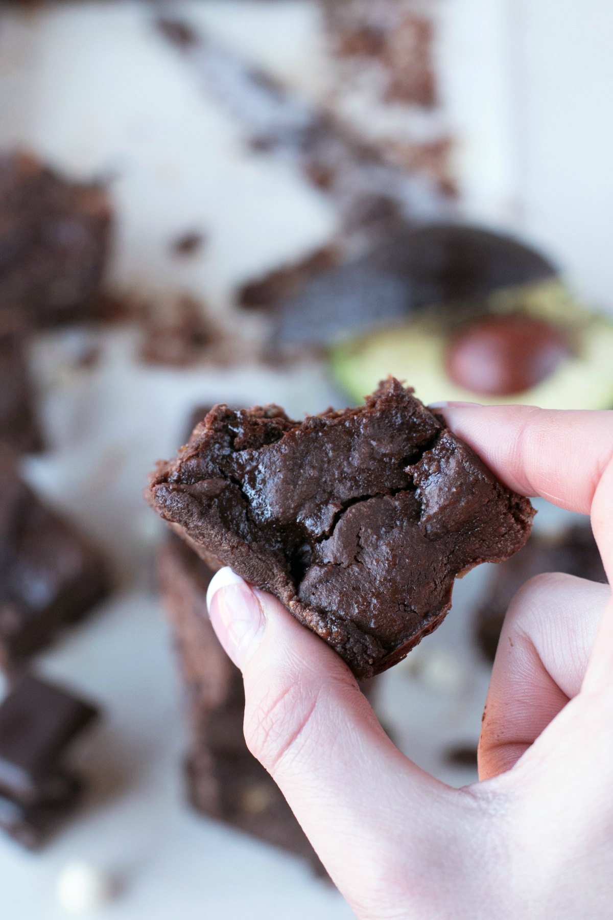 A hand holding a single avocado brownie with a bite out above other brownies in background