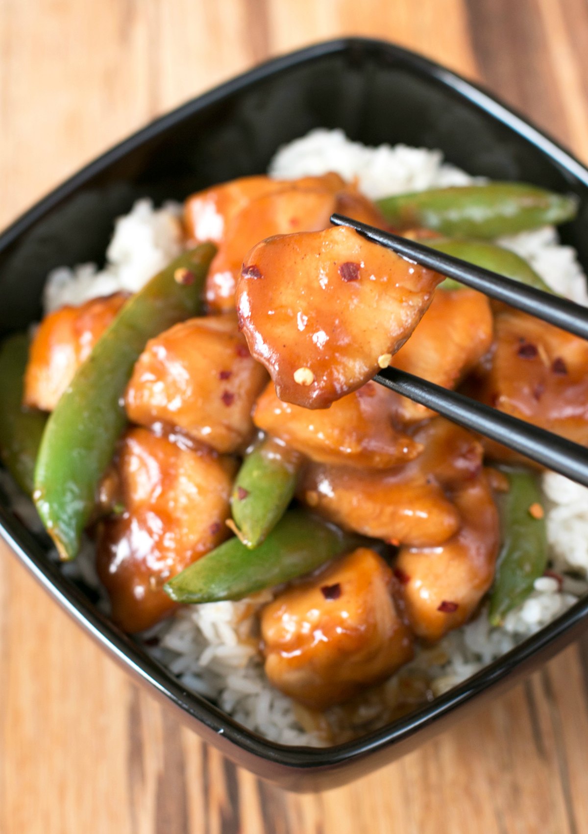 Chopsticks holding a piece of orange chicken recipe above a bowl