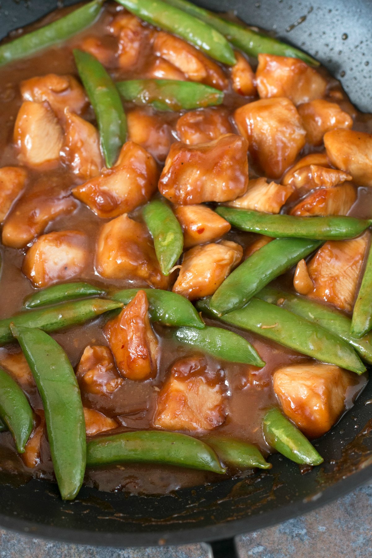 Orange chicken with pea pods in a wok being stir fried