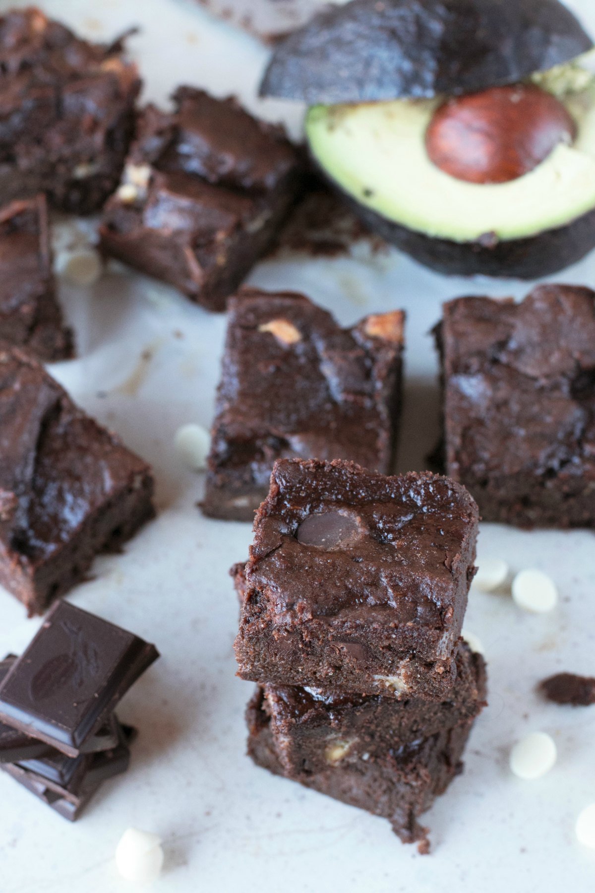 Overhead picture of a gluten-free dessert, brownies, stacked on parchment paper with avocado and chocolate chips in background
