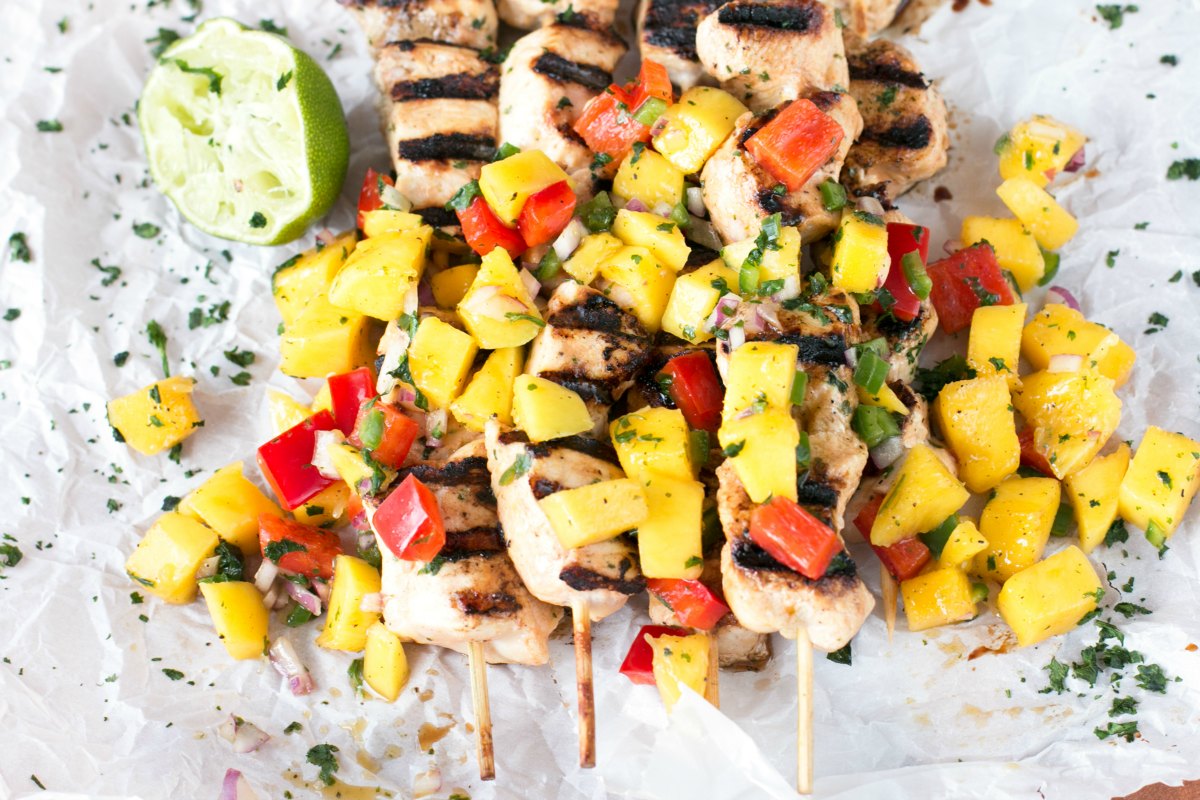 Overhead picture of mango chicken on kabobs with mango salsa and lime