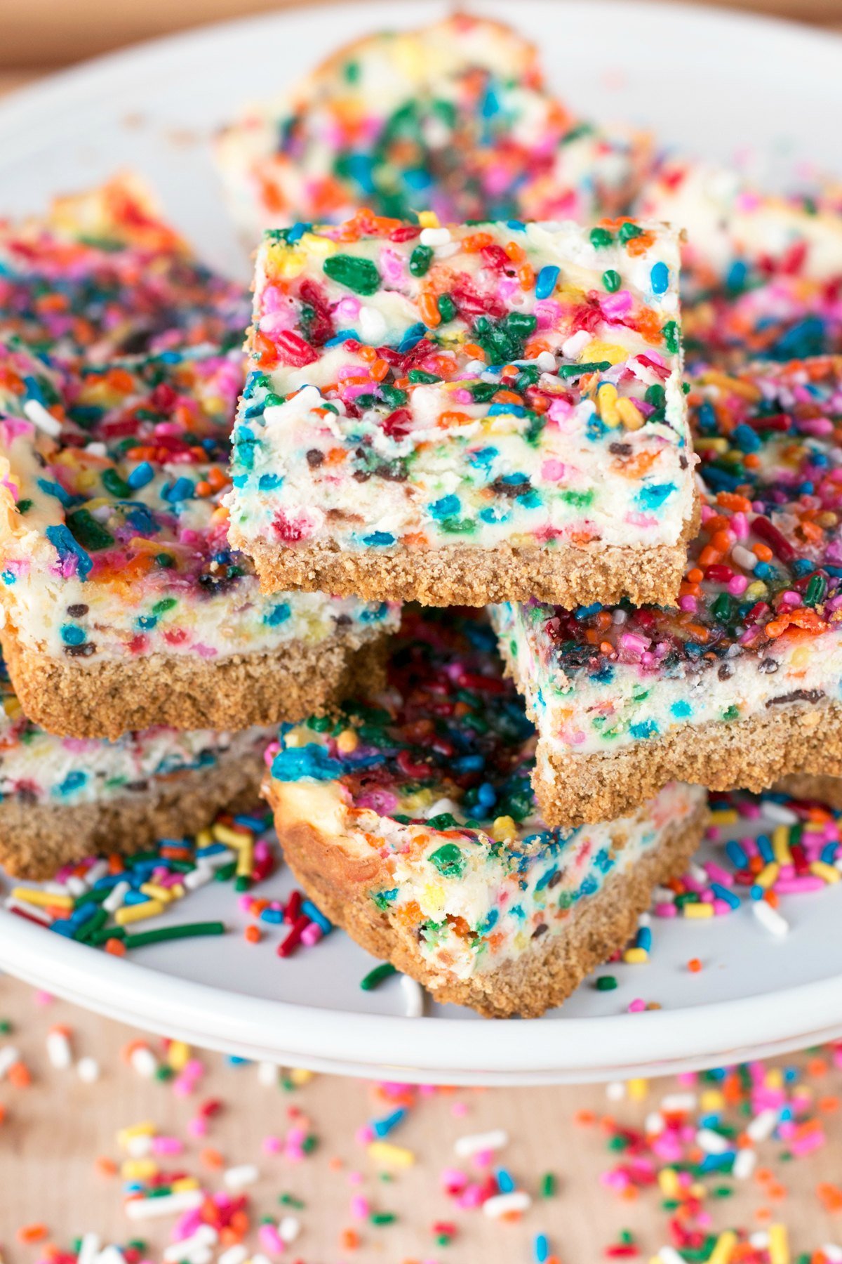 A white platter stacked high with funfetti cheesecake bars squares