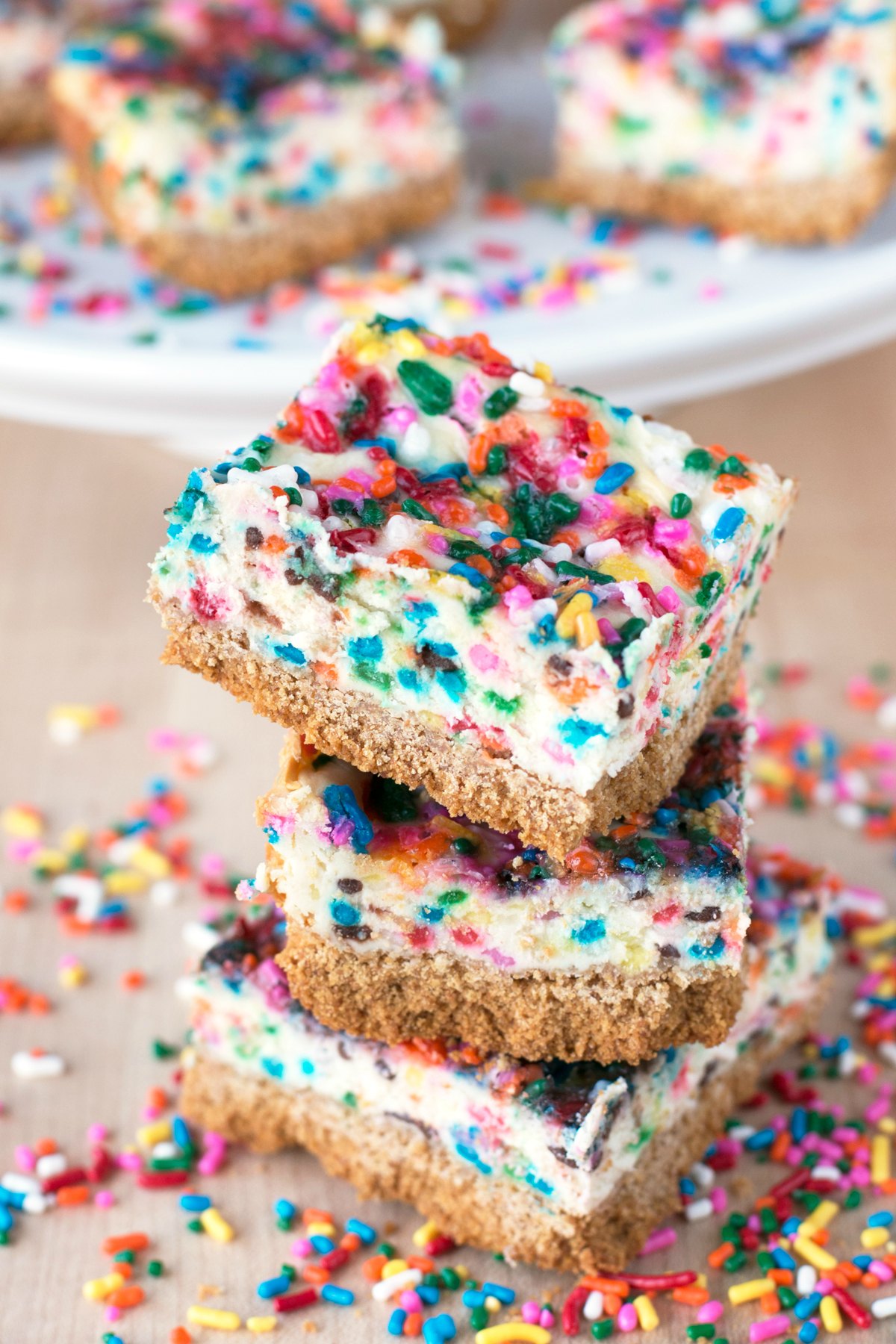 Three funfetti cheesecake bars stacked on a table and surrounded by spirnkles