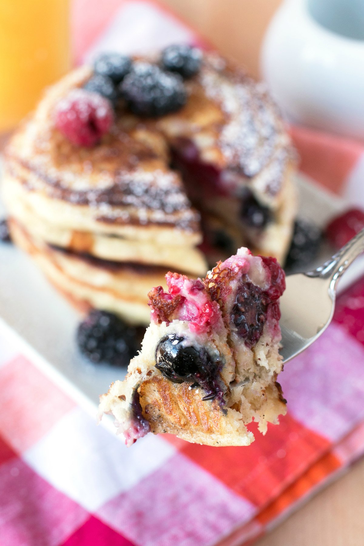 A fork full of mixed berry pancakes hovering over plate of pancakes