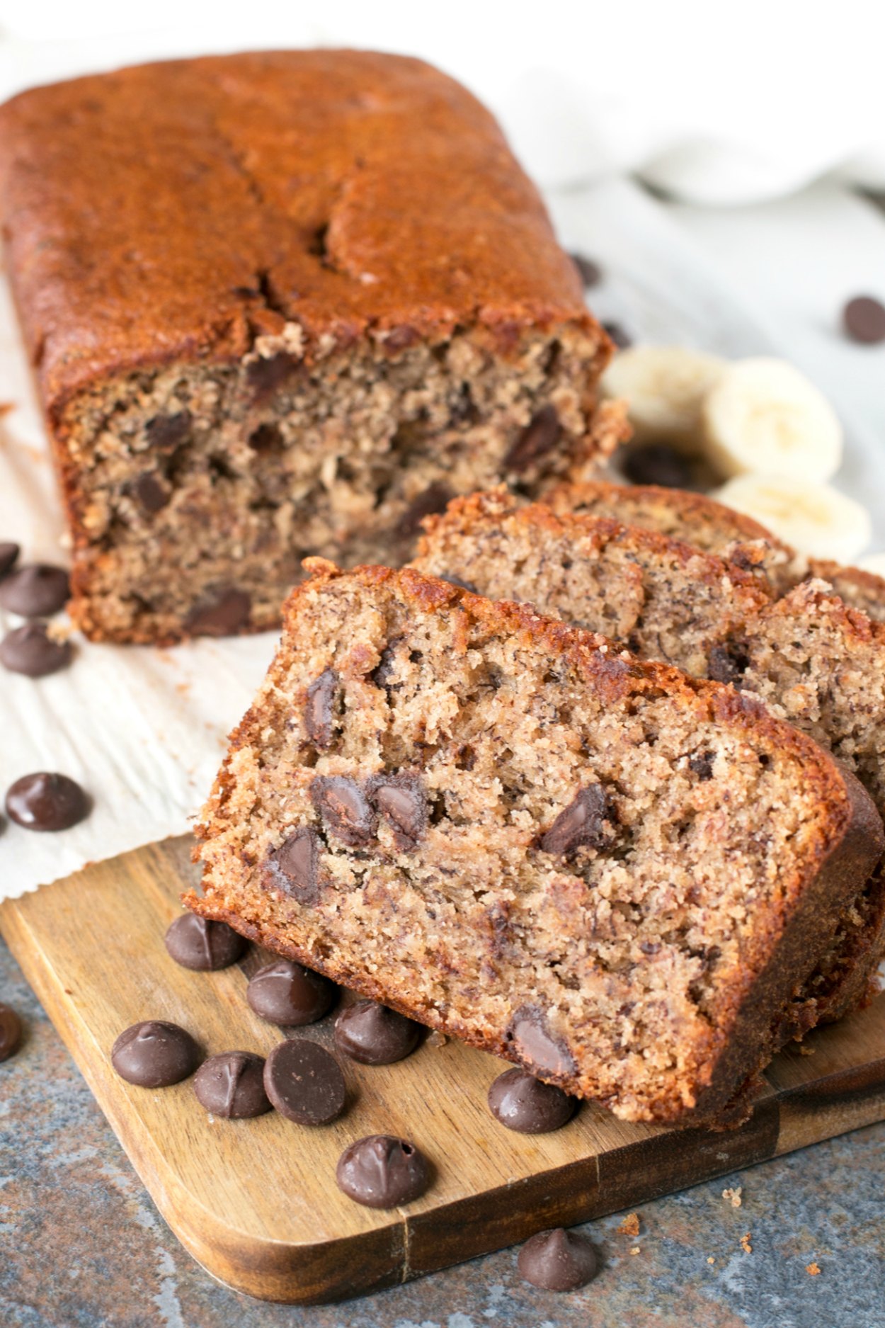 Loaf of chocolate chip banana bread with almond butter sliced and sitting on a cutting board