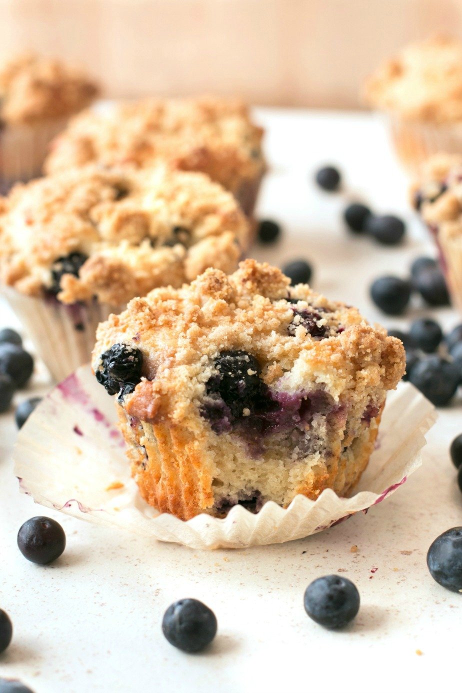 Blueberry crumb muffins sitting on a white surface with one having a bite taken from it