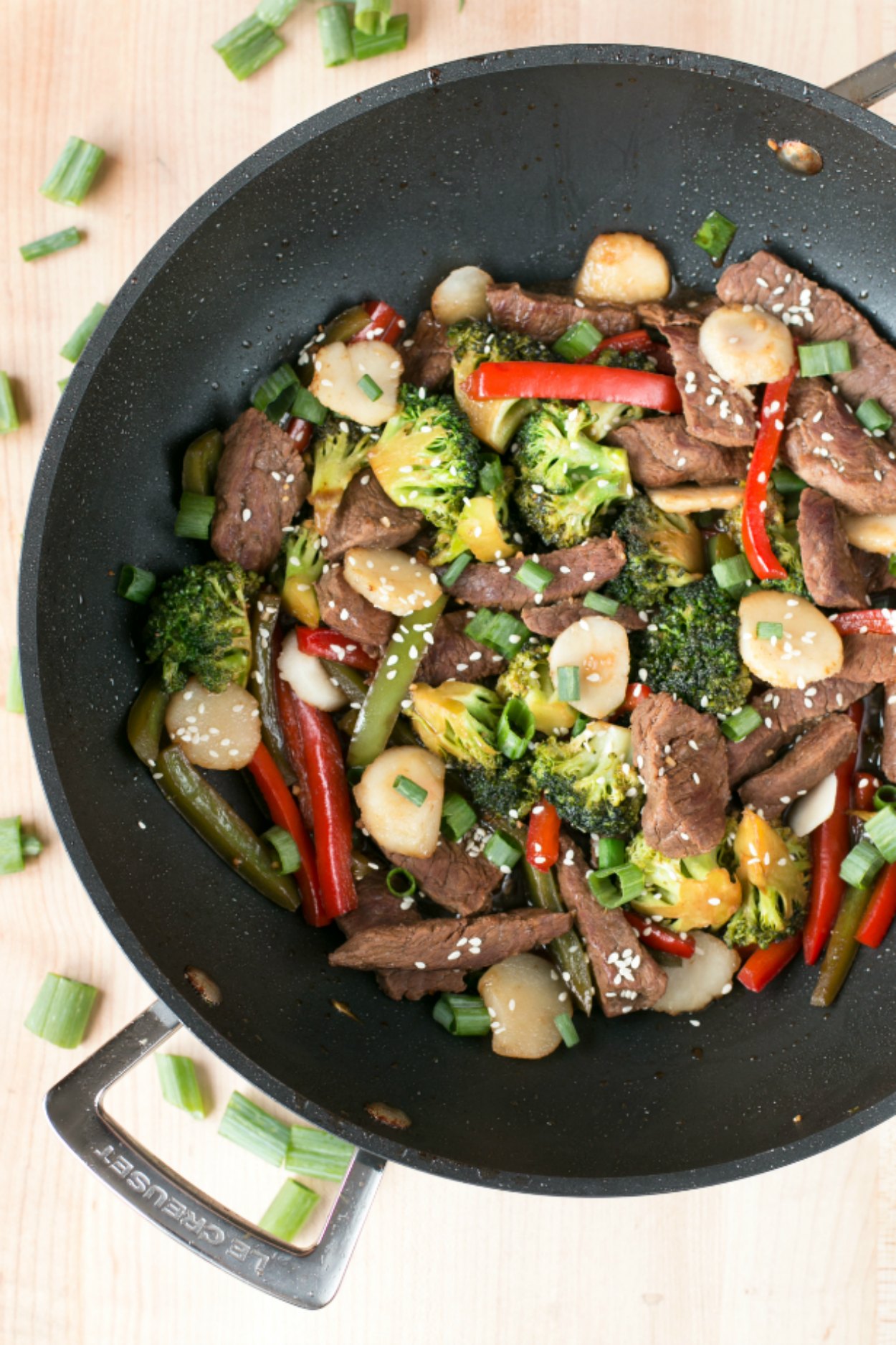 A large wok filled with beef stir fry and vegetables that is sitting on a wooden surface