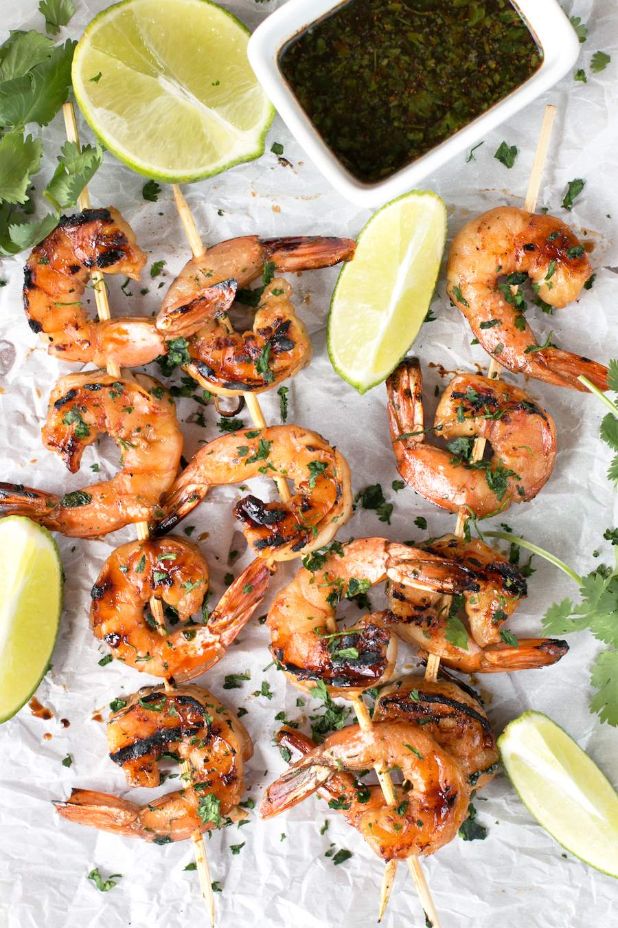 Agave Cilantro Shrimp Skewers with dipping sauce and lime on parchment paper.