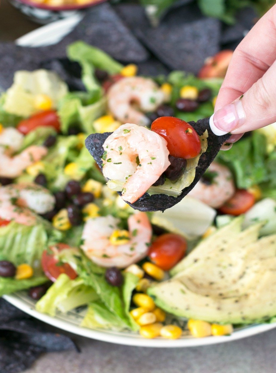 A single bite of Mexican Shrimp Taco Salad on a blue corn tortilla chip held by a woman