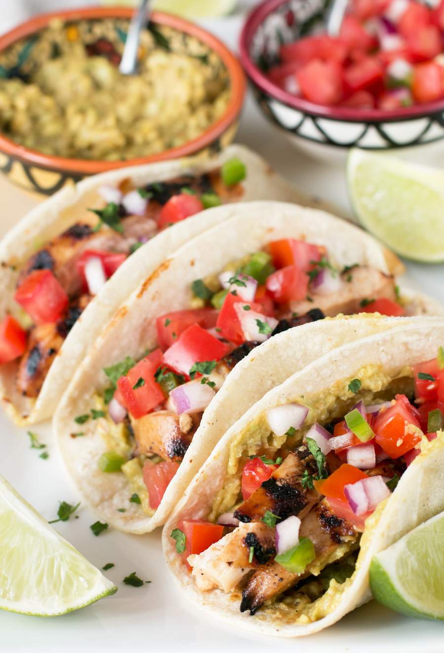 Three Mexican Chicken Tacos on a white plate in corn tortillas.