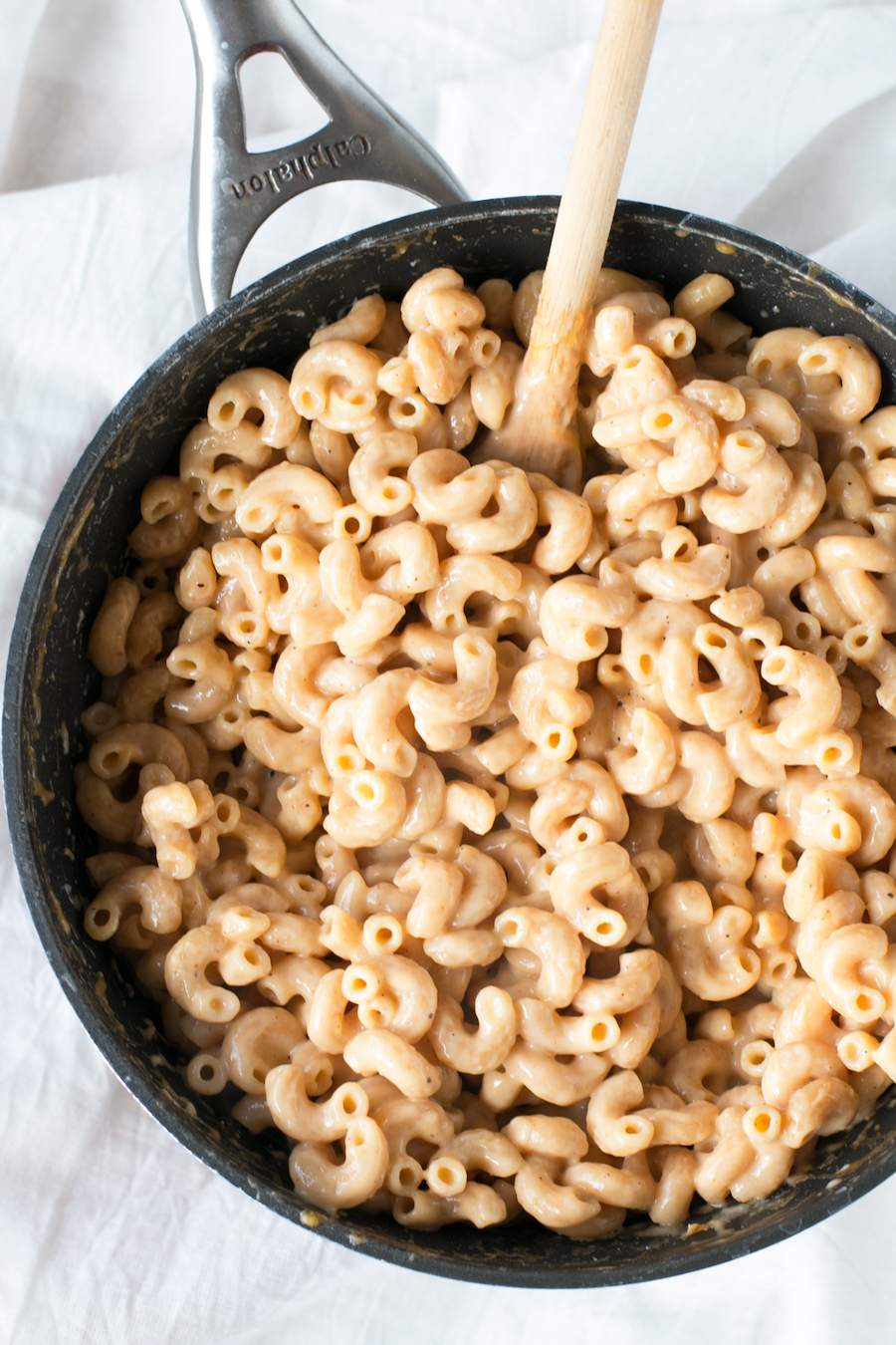 Sauce pan with One Pot Whole Wheat Macaroni and Cheese and a wooden spoon on a white tablecloth