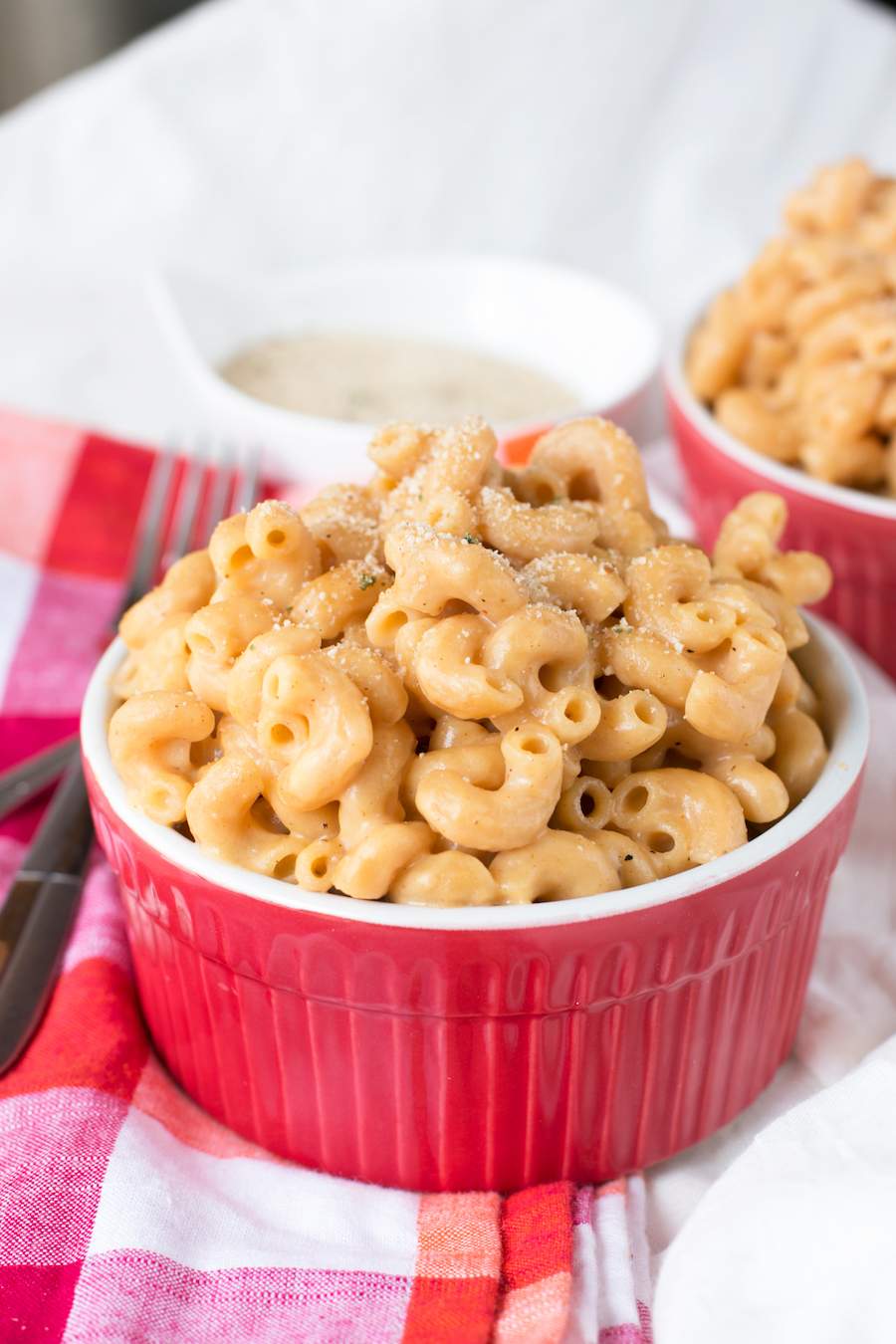 Two red ramekins of One Pot Whole Wheat Macaroni and Cheese  with forks on a white and red tablecloth