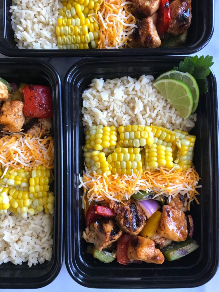 Boxes of meal-prepped lunches: Rice, fresh corn, cheese, and chicken shish kabobs