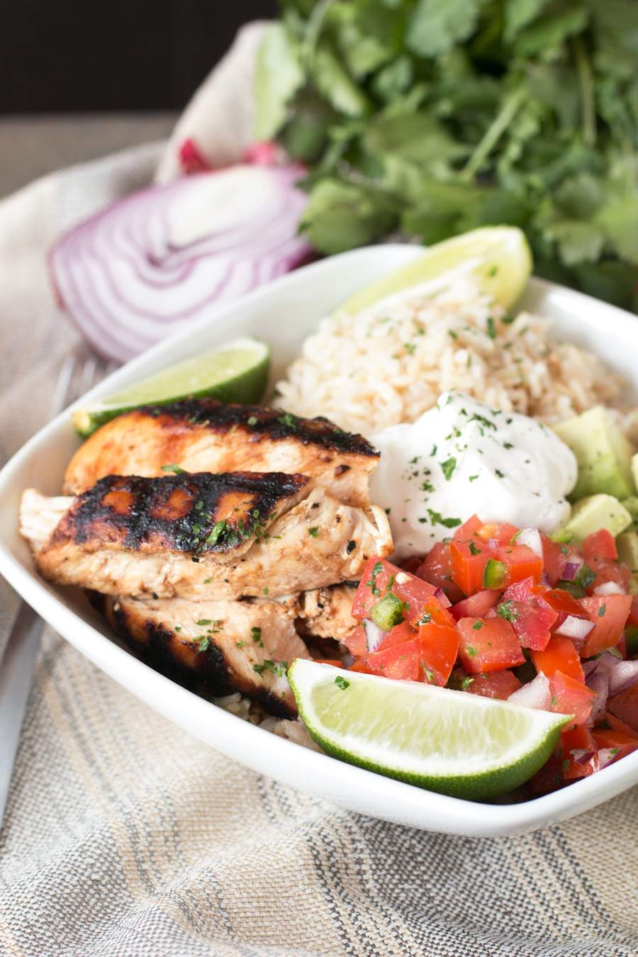 A white bowl of Grilled Chicken Burrito on a towel with herbs behind the bowl.