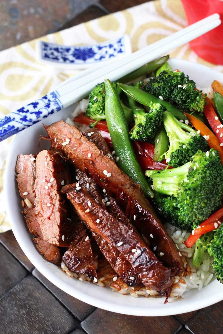 Image of soy marinated flank steak stir-fry with white and blue chopsticks on the bowl and a white and brown napkin in the back.