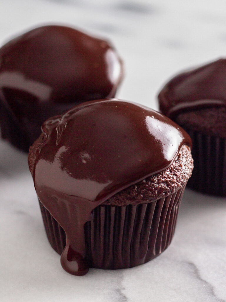 Three cupcakes with a chocolate ganache topping.