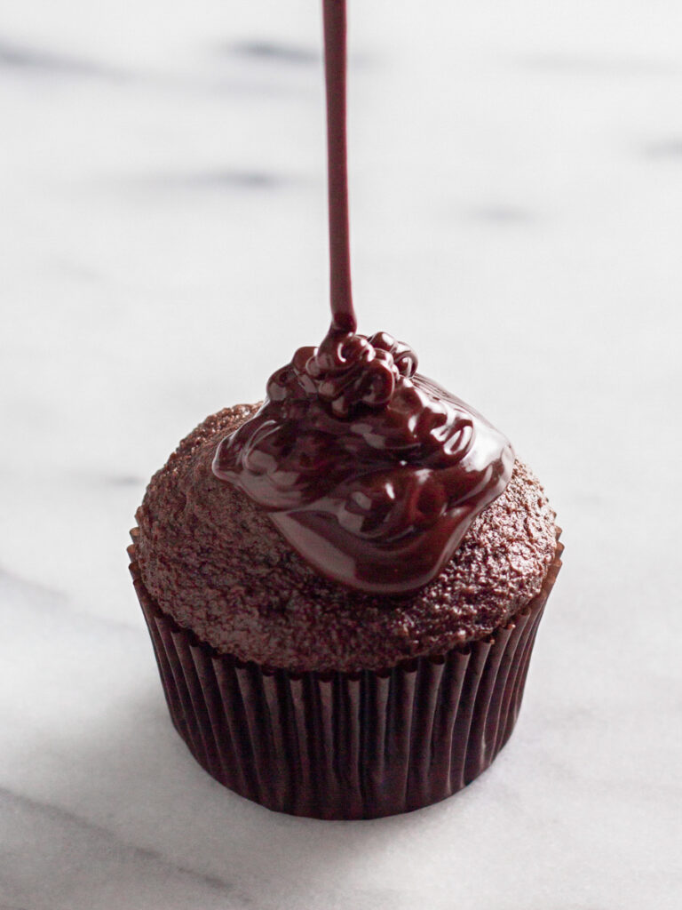 Chocolate ganache poured over a cupcake.