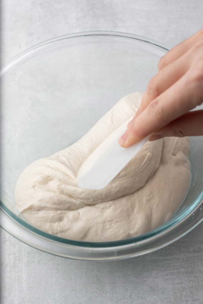 Folding ciabatta bun dough with a bench scraper.