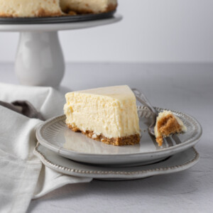 A slice of new york style cheesecake on a plate with the tip on the fork beside it.