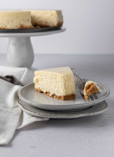 A slice of new york style cheesecake on a plate with the tip on the fork beside it.