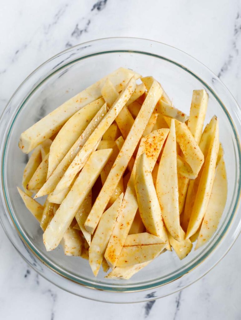 Coating sweet potato slices in a bowl. 