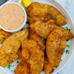 Chicken strips on a plate with sauce.