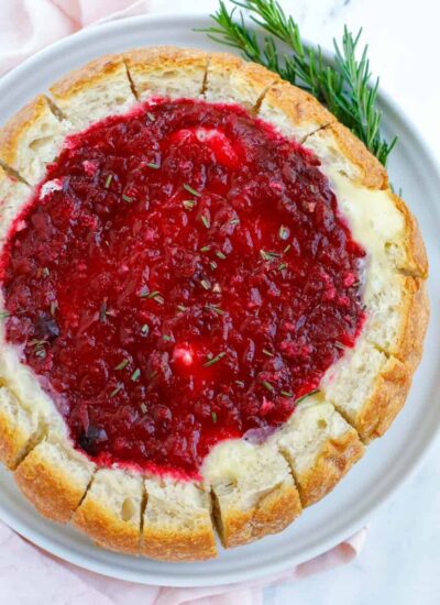 Top down view of baked brie cranberry bread bowl with herbs on the side.