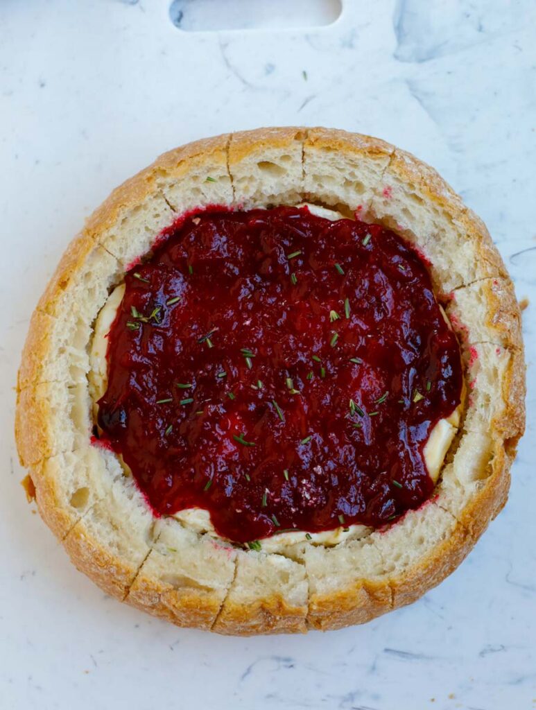 Cranberry sauce on top of brie in bread bowl and sides cut into