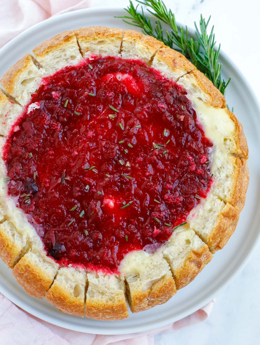Top down view of baked brie cranberry bread bowl with herbs on the side.