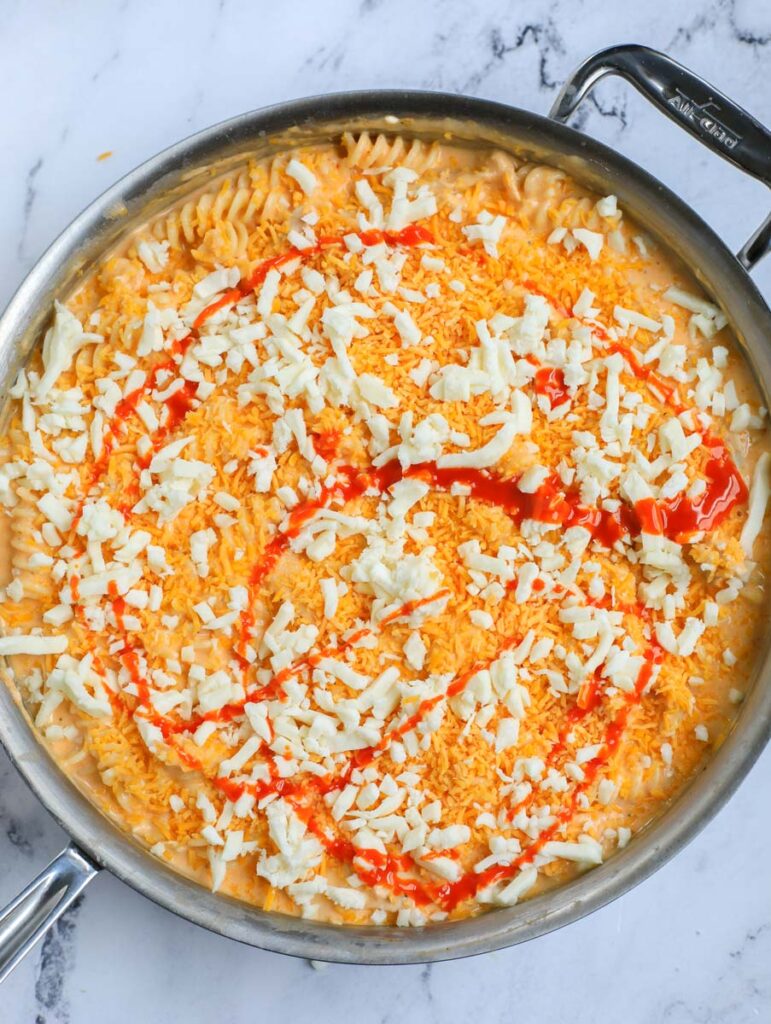 Buffalo sauce and cheese on top of pasta in a pot.