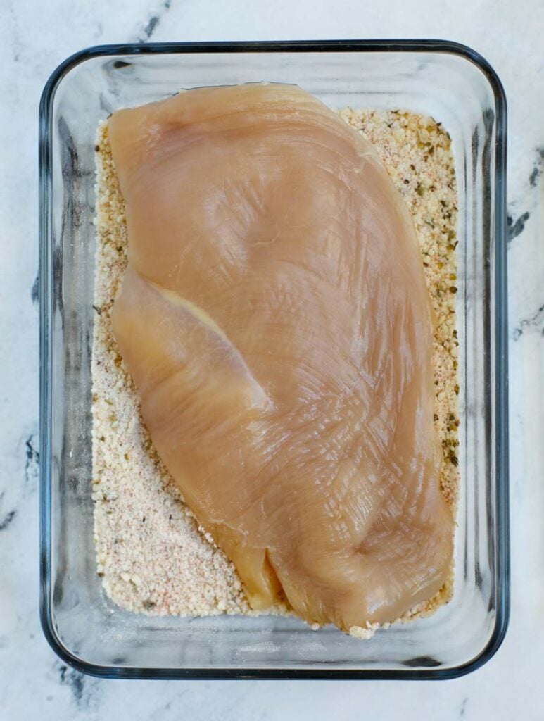 Chicken breast added to a container to be coated by flour and seasoning.