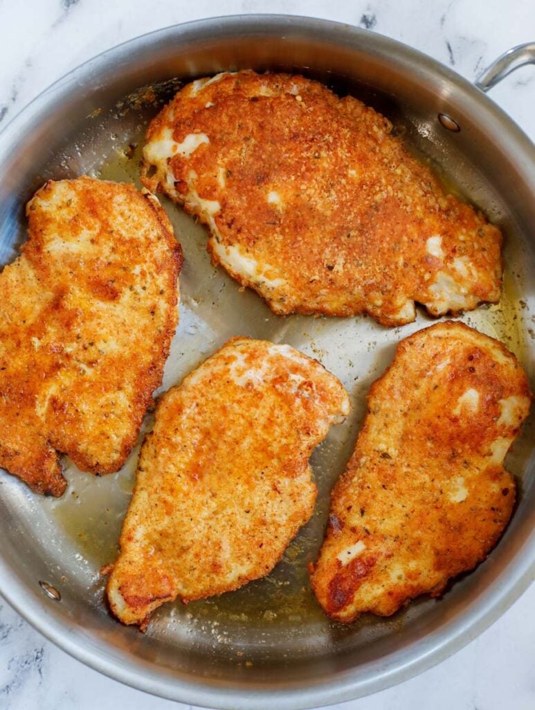 Chicken breasts pan fried in a skillet.