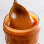 Close up of caramel sauce in a jar with a spoon.