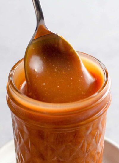 Close up of caramel sauce in a jar with a spoon.