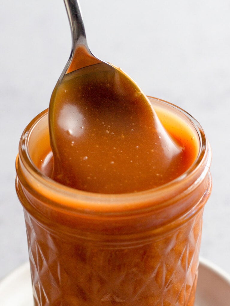 Close up of caramel sauce in a jar with a spoon.