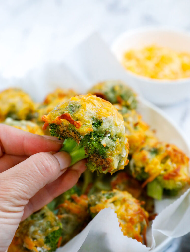 Hand holding a cheesy broccoli bite. 