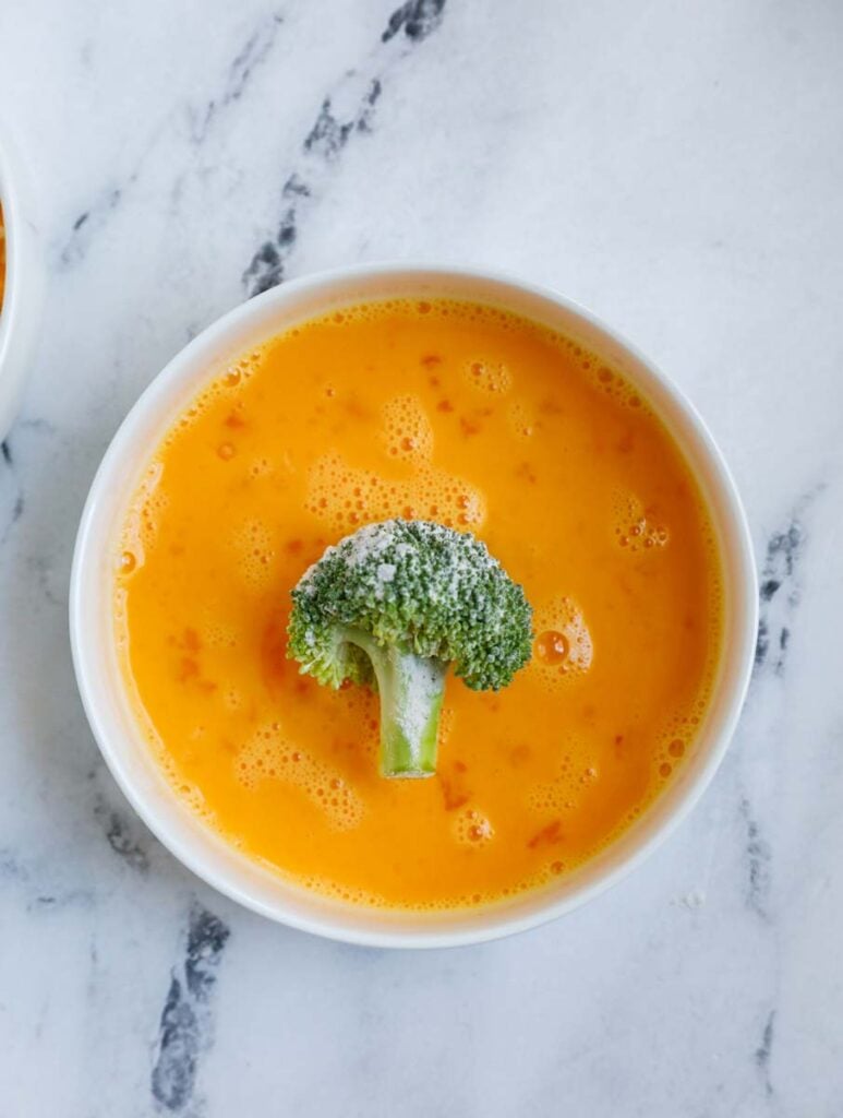 broccoli in a bowl of egg wash.