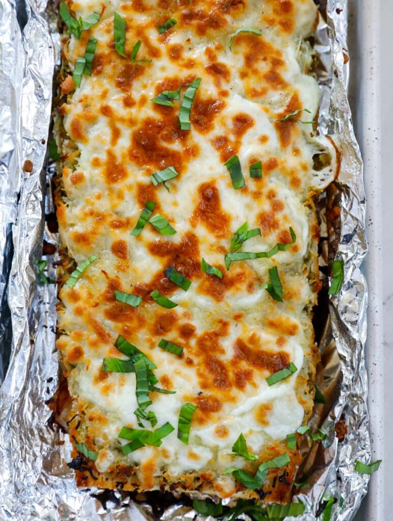 Top down shot of cheesy pesto breadstick surrounded with foil.