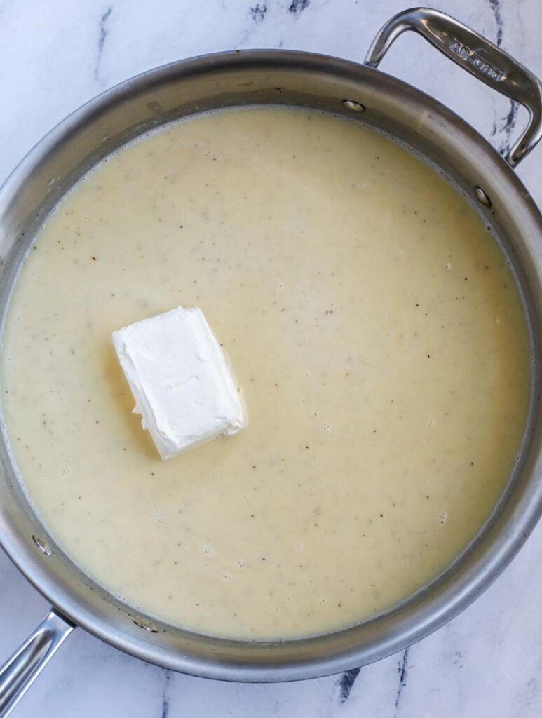 A stainless steel skillet with a creamy casserole sauce and a block of cream cheese.