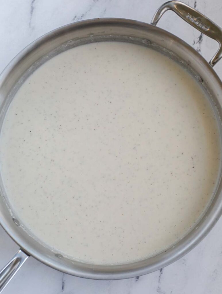 A large silver skillet with creamy casserole sauce on a marble counter.