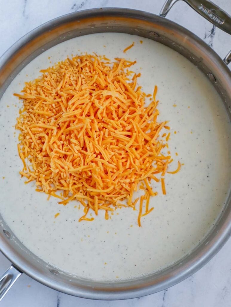 A silver skillet with a creamy sauce and a heaping pile of shredded cheddar cheese.