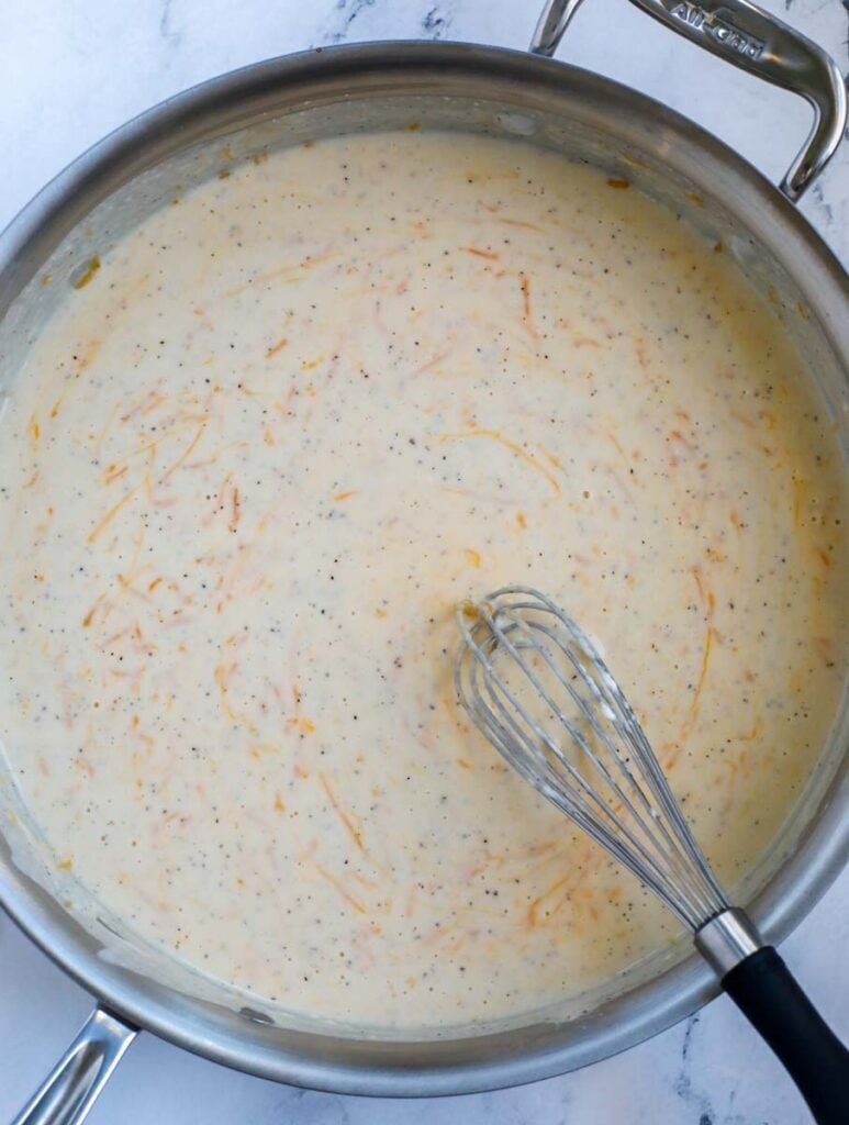 A silver skillet with a creamy, cheesy casserole sauce with a wire whisk on the right.