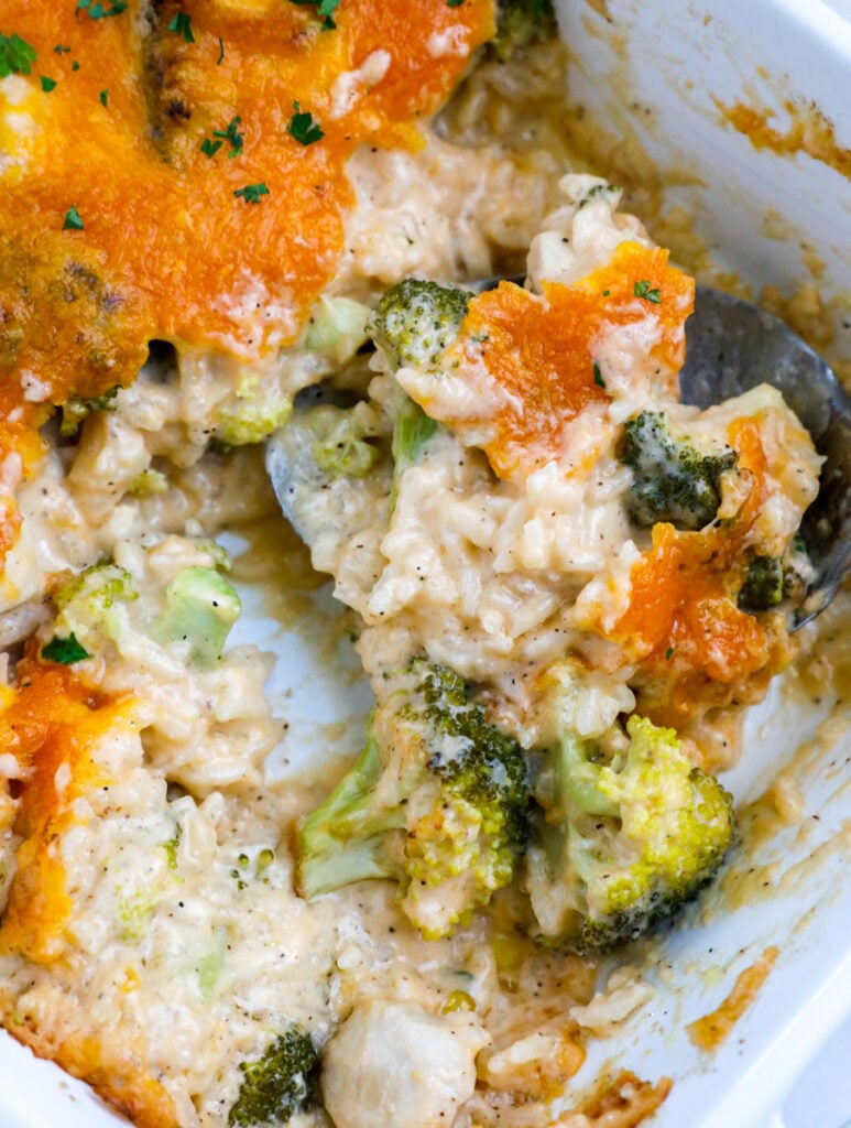 A scoop of chicken broccoli and rice casserole in a white baking dish.