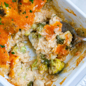 A white casserole dish with chicken broccoli and rice casserole topped with cheddar cheese on a white counter.