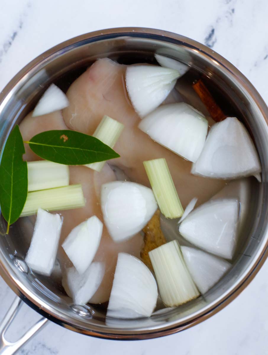 Chicken breasts inside of a pot and with onions and water.