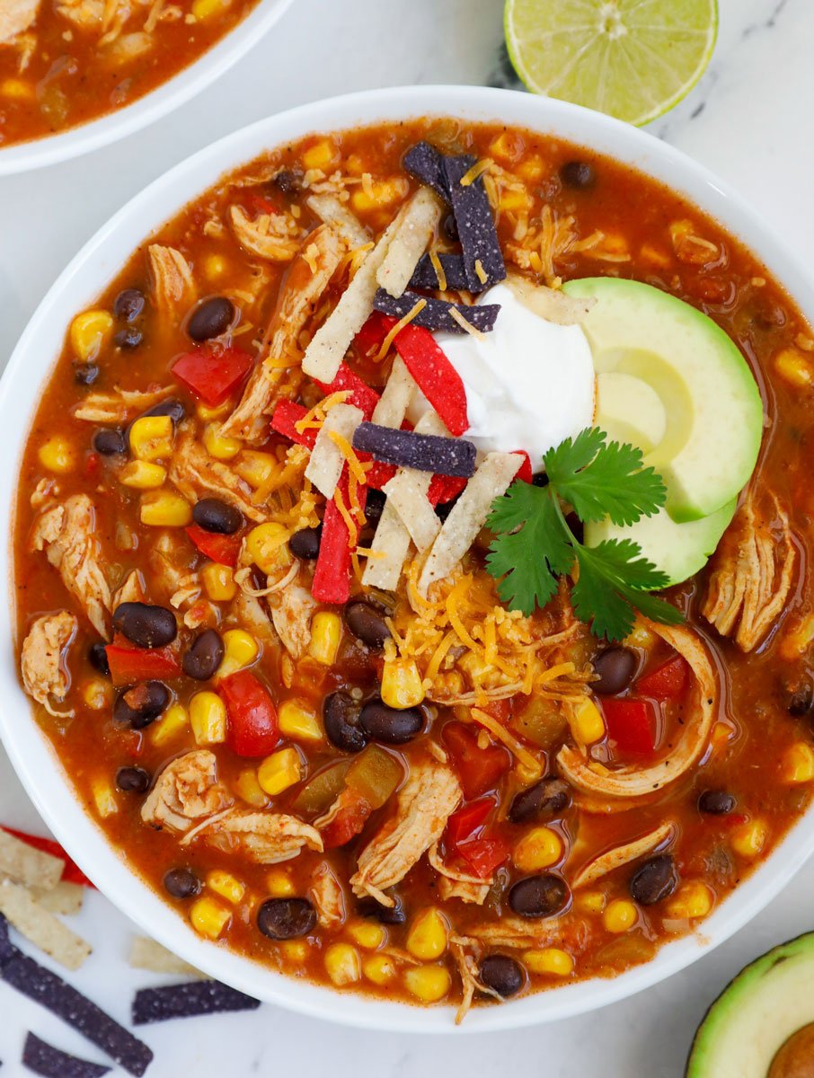 A top down photo of a bowl of chicken enchilada soup recipe served with some toppings.