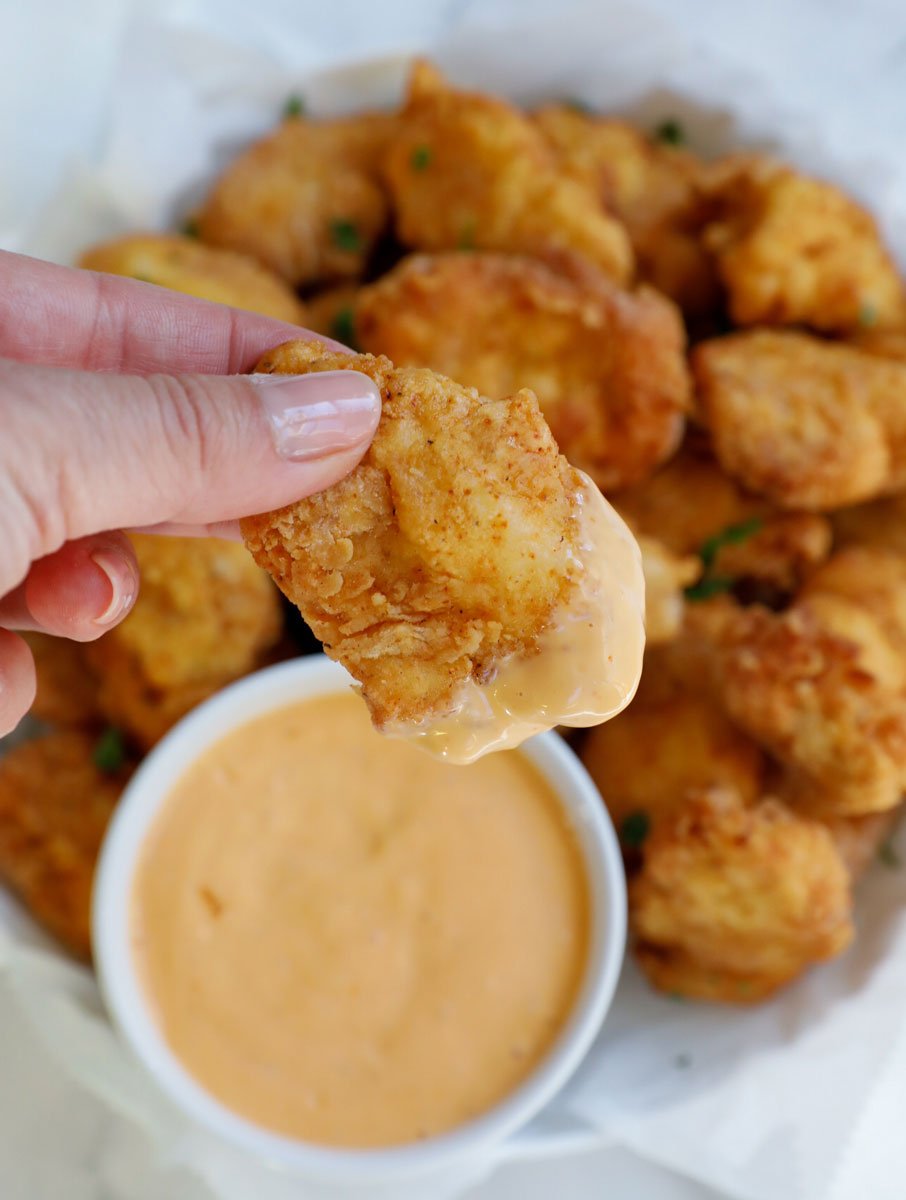 female hand holding a piece of chicken nuggets dipped in sauce