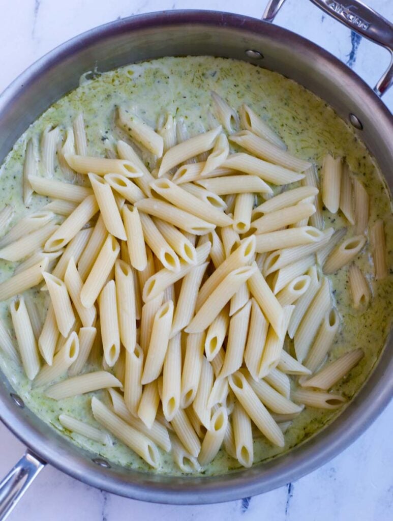 Cooked penne added to the sauce in a pan.