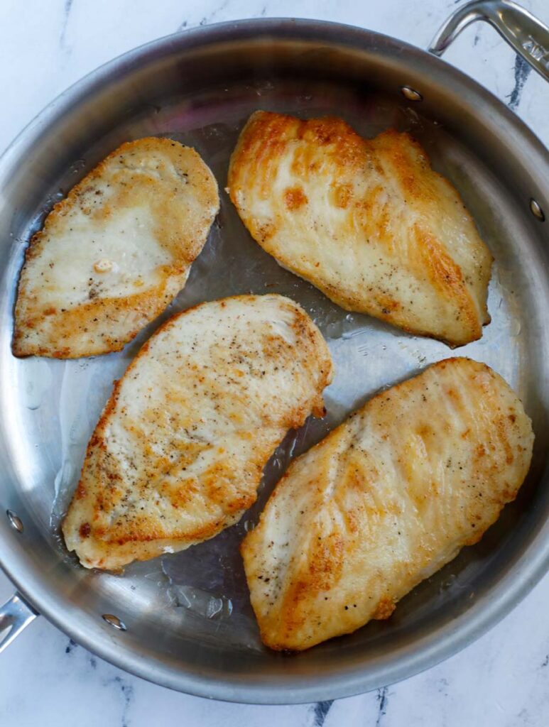 Pan frying chicken breasts in a pan.